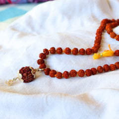 A brown rudraksha mala with a silver OM pendant on a white fabric surface