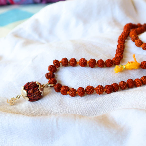 A brown rudraksha mala with a silver OM pendant on a white fabric surface